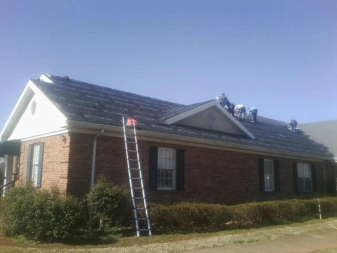 Crew tearing shingles off a brick ranch roof with a ladder set — Emergency Roof Repair work by our crew in Mascot
