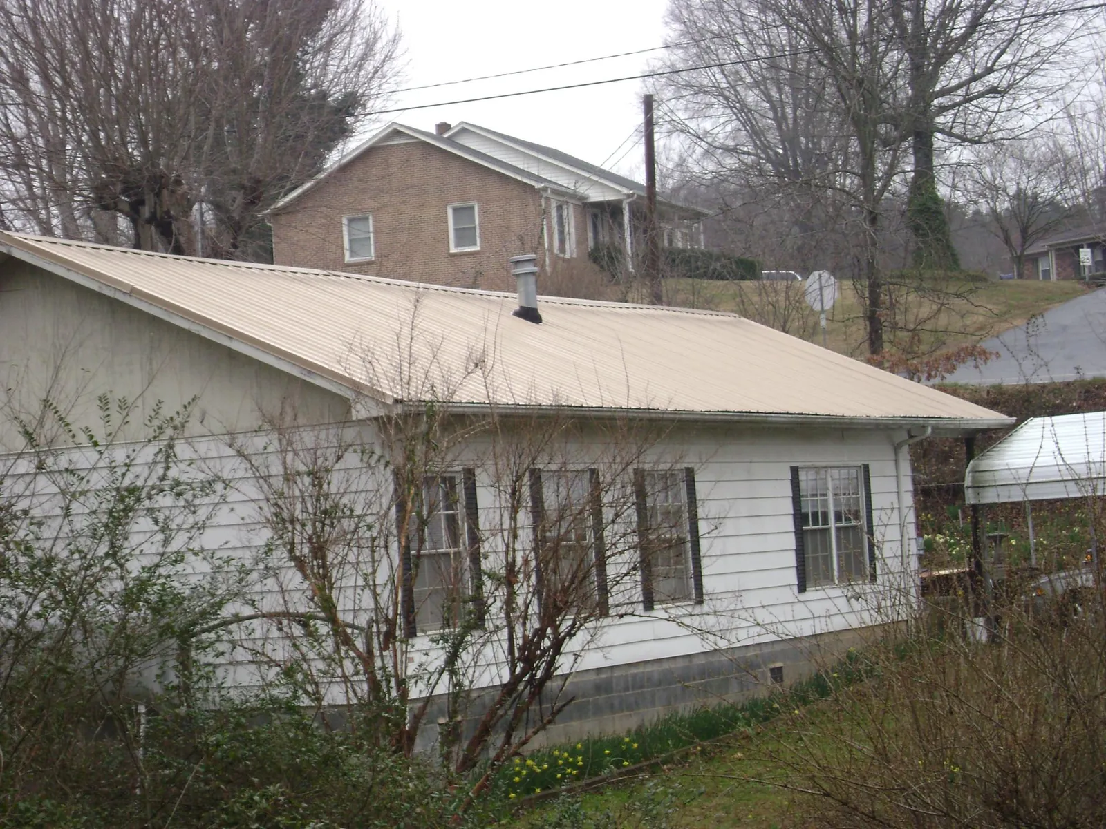 Tan metal roof on a white sided house set into a hillside — Commercial Roofing by Roofing Brothers in Mascot